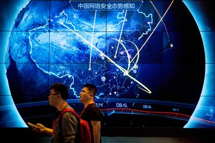 Asistentes pasan por delante de una pantalla que muestra ciberataques recientes en China, en la Conferencia de Seguridad en Internet, en Pekín, en septiembre de 2017. (AP Foto/Mark Schiefelbein, archivo)