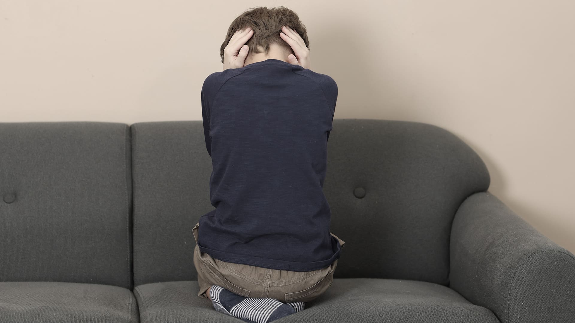Autism concept. Lonely little boy covering his ears on sofa at home, back view