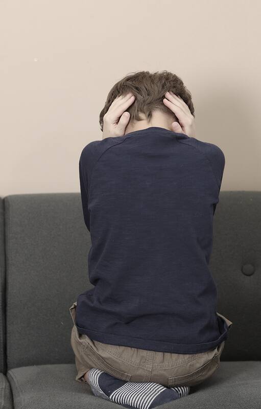 Autism concept. Lonely little boy covering his ears on sofa at home, back view