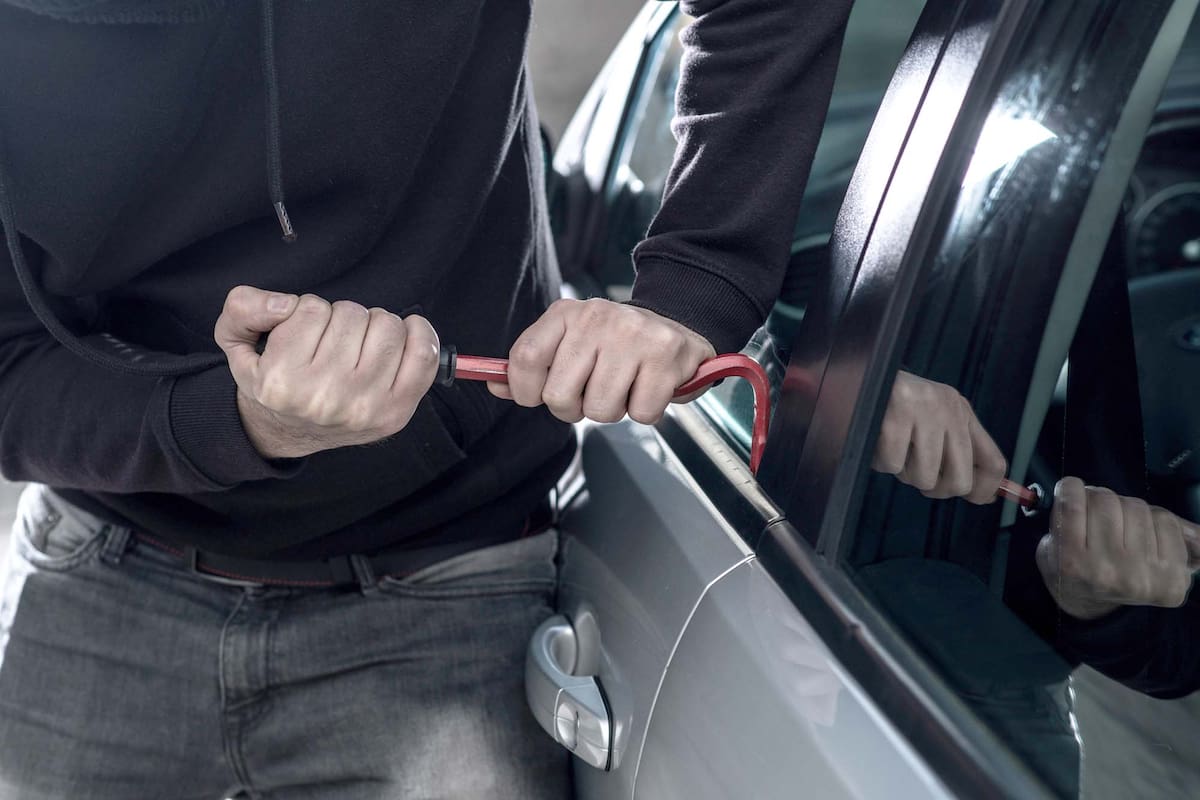 Auto thief in black balaclava trying to break into car with crowbar. Car thief, car theft