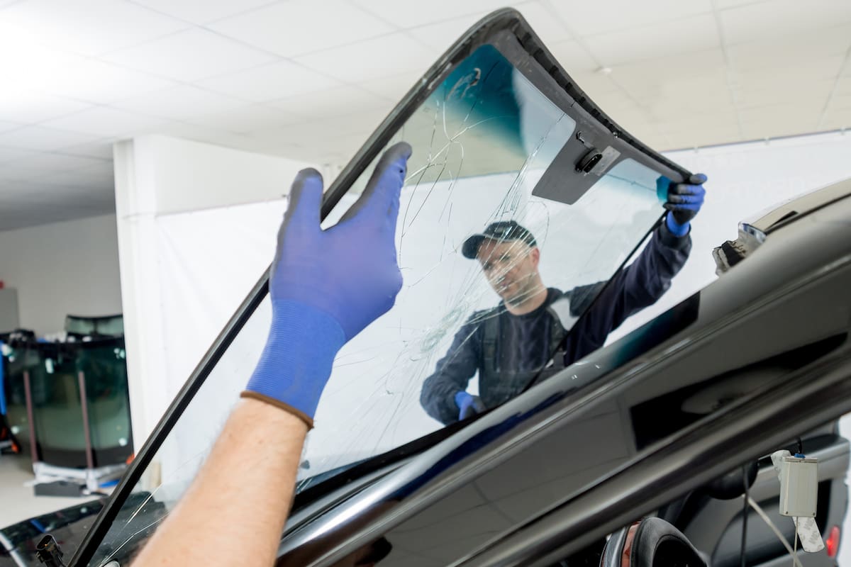 Automobile special workers remove old windscreen or windshield of a car in auto service station garage. Background
