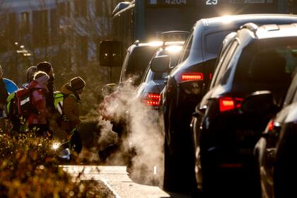 Automóviles emiten gases de escape mientras niños caminan a una escuela de Fráncfort, Alemania, el lunes 27 de febrero de 2023. (AP Foto/Michael Probst)