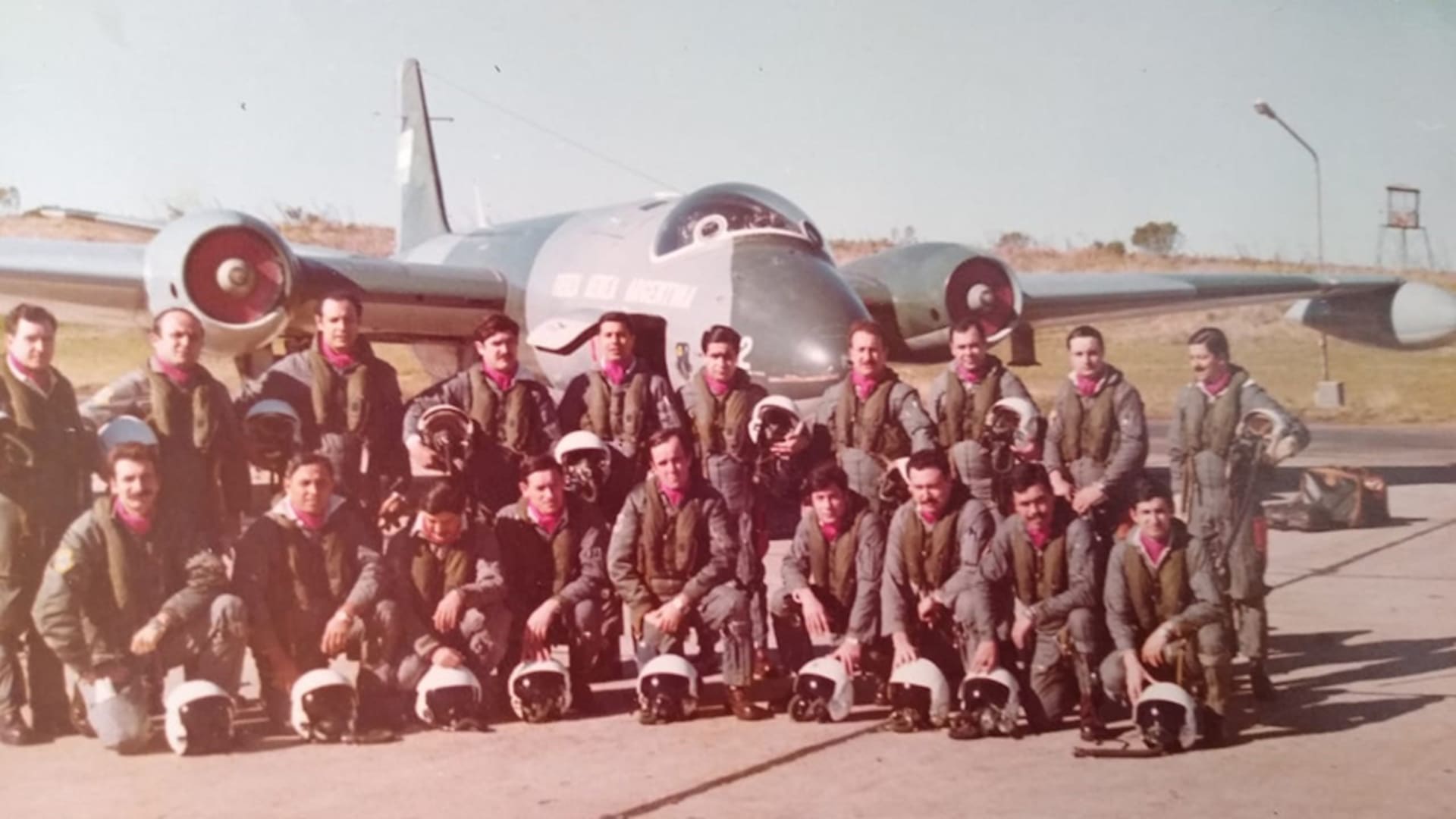 Aviadores argentinos con el pañuelo bordó en su cuello, que era distintivo del Escuadrón Canberra; en el fondo, un avión Canberra