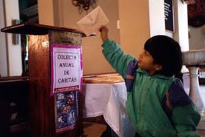 Ayer, un chico pone un sobre para la colecta de Caritas en la parroquia Nuestra Señora del Socorro, Juncal y Suipacha
