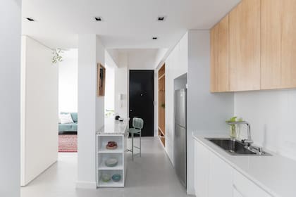 Bacha (Johnson), grifería (FV). En el extremo de la barra, un módulo de madera laqueada blanca. Como es un ambiente interno, la propuesta de iluminación incluye spots empotrados (Vita Arquitectura). Al fondo, la puerta de entrada pintada de negro..