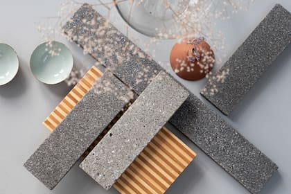 Baldosas BioBasedTiles® desarrolladas por Biomason y FRONT, fabricadas con biocemento mediante un proceso de cultivo a partir de microorganismos. Estos actúan como “obreros biológicos” que endurecen los agregados a temperatura ambiente, eliminando el uso de hornos y reduciendo a cero las emisiones de CO2