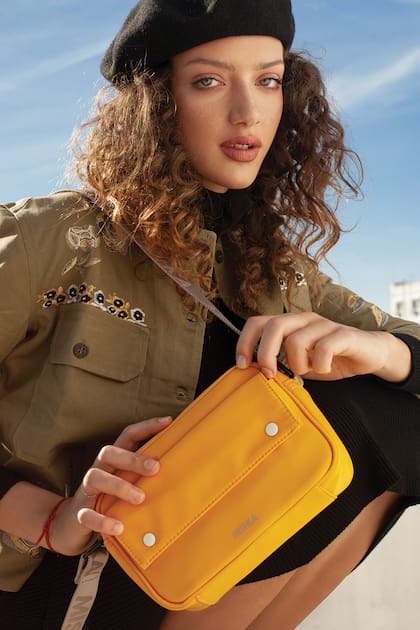 Bandolera rectangular de nylon amarillo (Mishka), boina (Renner), camisa verde con bordado en hilos metalizados (Rapsodia), vestido de calce recto y cuello polera (Renner)