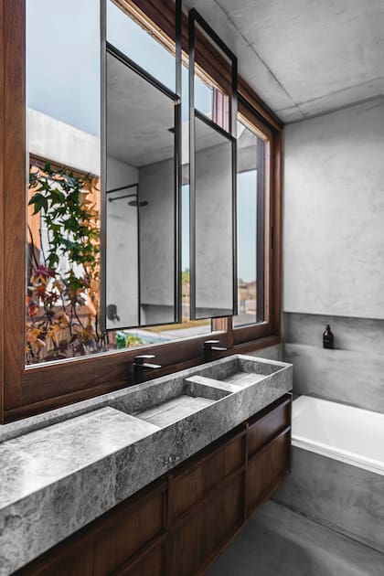 Baño con amoblamiento enchapado en petiribí y bacha armada en mármol ‘Gris Emperador’ (Venato Mármoles), el mismo que se usó en la cocina. Grifería ‘Epuyén’ (FV). Espejos montados en una estructura de hierro colgada de la losa estructural por delante del ventanal que da al patio.
