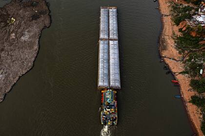 Barcazas cargadas de cemento navegan por el canal entre la playa y un antiguo volcán extinto, expuesto por el bajo nivel del río Paraguay, en Asunción, en medio de una histórica sequía que está afectando su nivel, el miércoles 22 de septiembre de 2021. (AP Foto/Jorge Saenz)