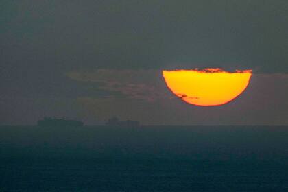 Barcos navegan por el golfo Pérsico hacia el estrecho de Ormuz mientras se pone el sol en Emiratos Árabes Unidos