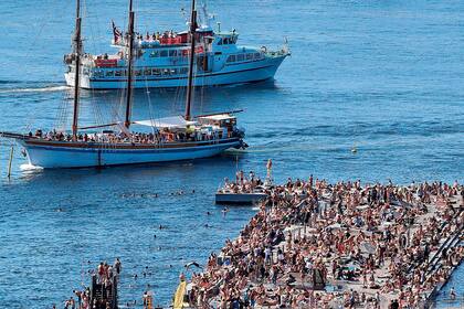 Barcos pasan frente a la concurrida zona de baño en Sorenga, Oslo, en la piscina interior del puerto de la capital noruega