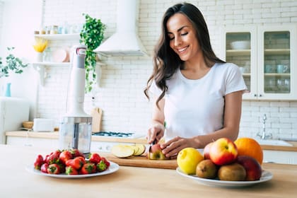 Beautiful woman making fruits smoothies with blender. Healthy eating lifestyle concept portrait of beautiful young woman preparing drink with bananas, strawberry and kiwi at home in kitchen.
