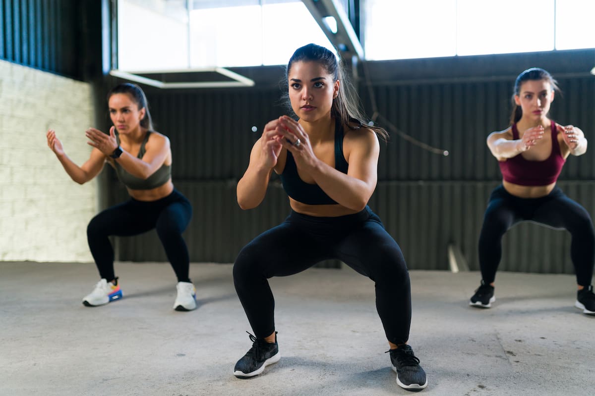 Beautiful women doing a cardio HIIT routine and squatting. Three fit women in sportswear working out and doing squats in the gym