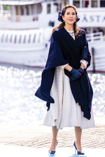 Bellísima, la reina danesa bajó del barco con un vestido de tweedblanco con falda con vuelo de Mark Kenly Domino Tan, que combinó con accesorios en azul: capa (que se quitó apenas puso un pie en tierra), stilettos Gianvito Rossi, clutch de Quidam, guantes de piel y tocado de Jane Taylor con gran moño.