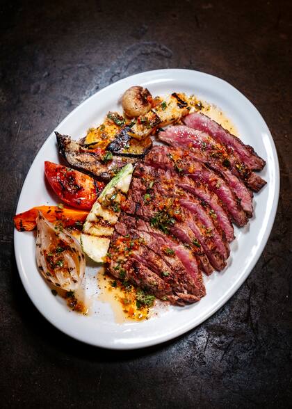 Bife ancho asado lentamente a la parrilla "al punto perfecto" con chimichurri y vegetales ahumados, uno de los más pedidos de la casa