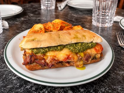 Bife de chorizo en pan chapata de elaboración propia, con carne cortada en finas láminas, pesto de albahaca, tomate asado, cebolla caramelizada y queso fundido