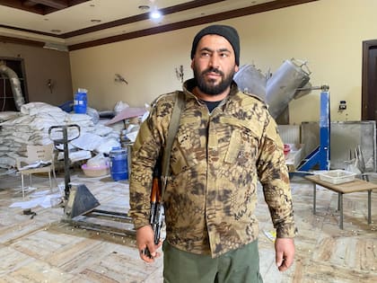 Bilal, el miliciano que controla la fábrica, de pie con su kalashnikov al hombro, vestido con camuflaje y un gorro negro, vigilando desde la entrada de la mansión.