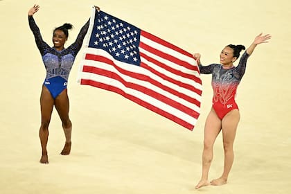Biles y Lee sostienen la bandera de Estados Unidos tras obtener las medallas dorada y bronce en All Around en el Bercy Arena de París, en un ajustado desenlace.