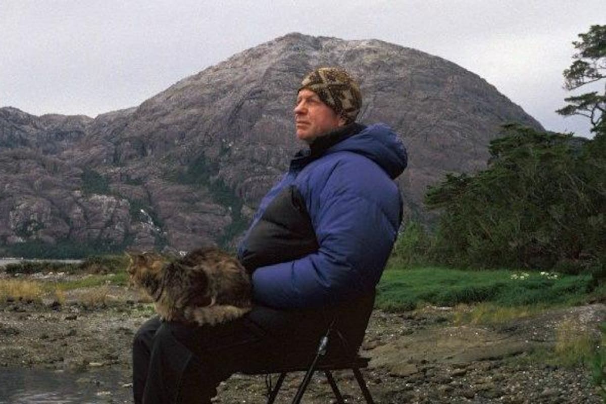 Bob Kull sentado en un silla con su gato en el regazo en la Patagonia chilena