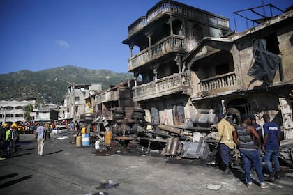 Bomberos están parados junto a los restos de un camión que trasportaba gasolina después que volcó y estalló en Cabo Haitiano, Haití, martes 14 de diciembre de 2021. La explosión mató a más de 50 personas y causó lesiones a varias decenas. (AP Foto/Joseph Odelyn)