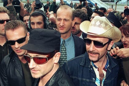 Bono junto al guitarrista The Edge y el baterista Larry Mullen Jr. rodeados de periodistas mientras avanzan por el aeropuerto de Sarajevo el 23 de septiembre de 1997