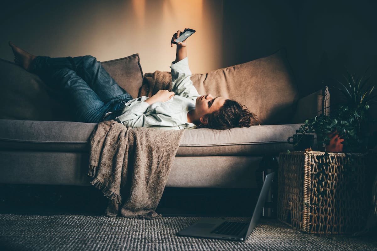 Bored woman in self isolation laying on the sofa. Woman in quarantine for coronavirus working from home.