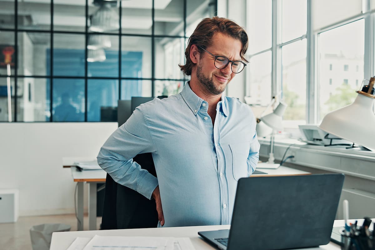 Business, man and laptop with back pain in office from bad posture, muscle injury and software mistake. Discomfort, male person and spine inflammation with IT pressure, employee burnout and stiffness