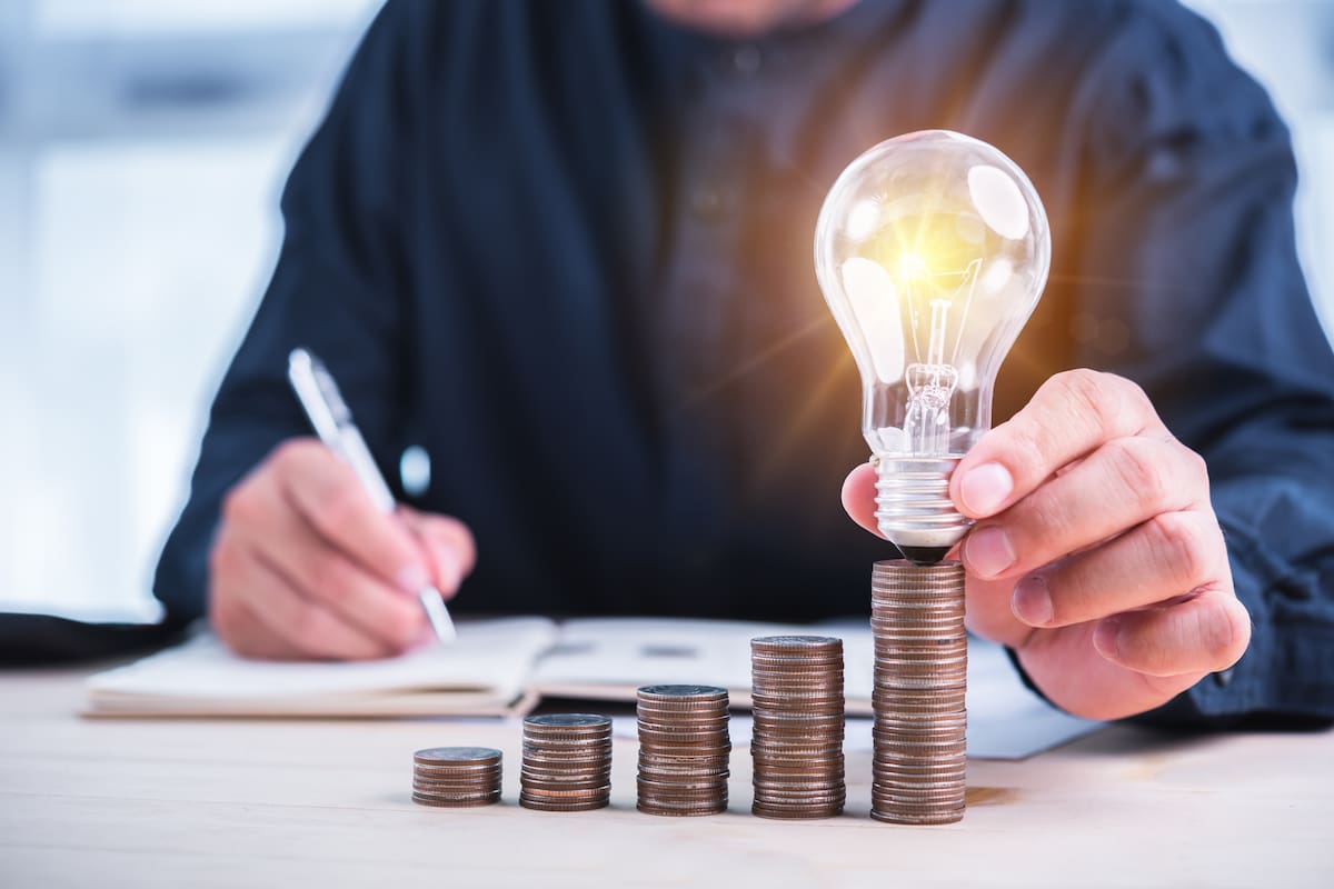 businessman hand holding lightbulb with coins stacking on desk.saving energy and money concept.