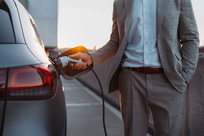 Businessman, holding power supply and charging his electric car during sunset. Concept of ecology tranport.