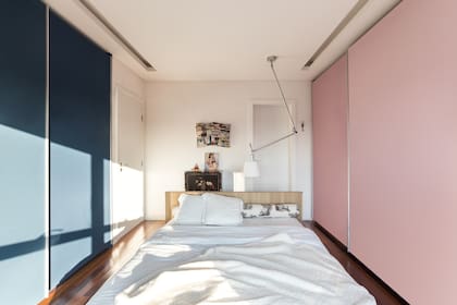 Cama baja (Aline Roman Arquitetura) de madera de tauarí, ubicada en el centro de la habitación. A los lados, las puertas corredizas de los placares pintadas de azul y rosa.