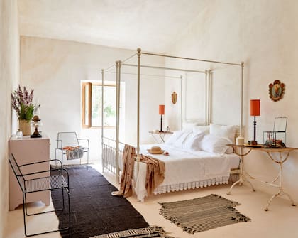 Cama con baldaquino, acertada para ambientes altos y, como mesa de luz, una vieja mesa de jardín francesa.