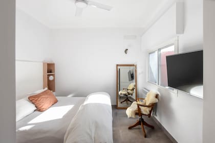 Cama con cajones en la base, mesa de noche empotrada de paraíso en crudo con cabecera laqueada en blanco (Estudio MPB), espejo con marco de roble comprado en una casa de antigüedades y sillón giratorio, también de roble, de herencia familiar.