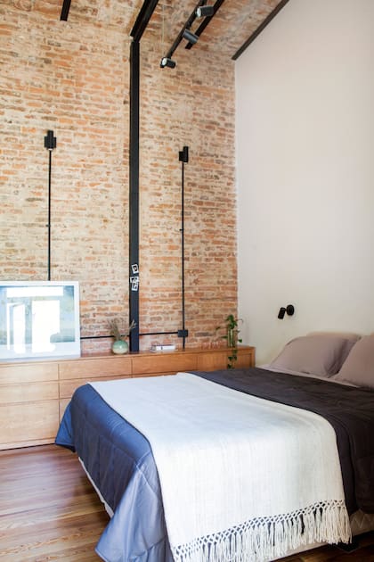 Cama con manta ‘Yavi’ (Elementos Argentinos), consola diseñada a medida (Estudio Yama). Luminarias de aluminio negro microtexturado (Paraná 201), montadas sobre apliques de pared.