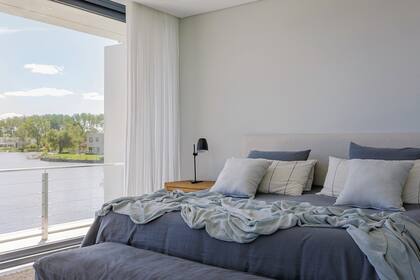 Cama con respaldo forrado en lino (De Levie) y almohadones (En Abundancia), mesa de luz ‘Simón’ de petiribí (Negro House Pleasures) y banco al pie con funda en canvas gris (Sol Palou).