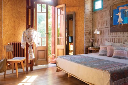 Cama de madera de guatambú (Carlos Lisjack) con manta, pie de cama, almohadas y almohadones (todo de Huitrú), mesa de luz heredada. Silla (DKP by Euge Zavaroni), antiguo radiador recuperado (Luis Erramuspe), kimono (The Kimono Life) y aberturas de demolición (El Mojón).