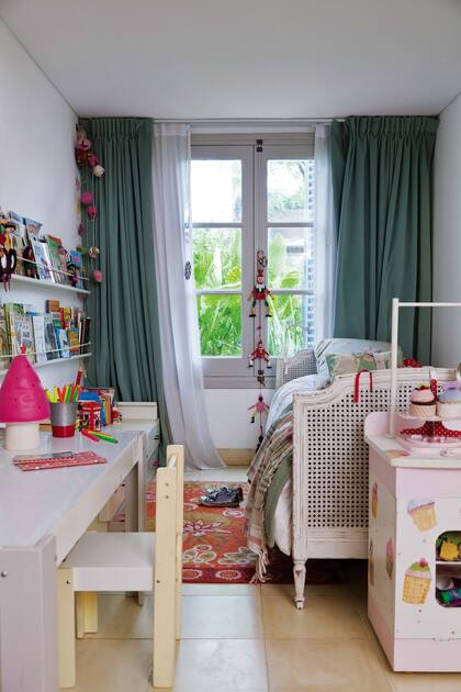 Cama provenzal, estantes de chapa pintados de blanco para los libros y una alfombra colorida para este cuarto alegre y acogedor.
