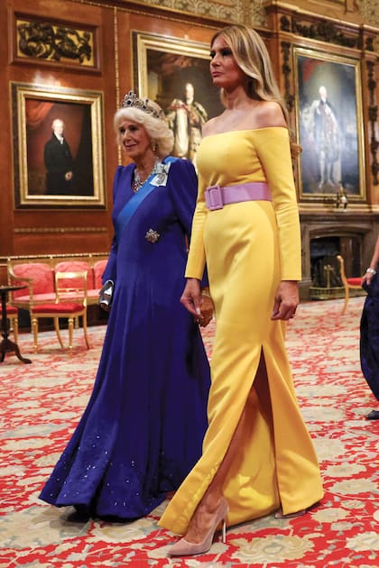 Camilla lució la tiara Belgian Saphire, de zafiros engastados en diamantes, que es una de las más espectaculares del joyero de los Windsor y volvió a elegir a la diseñadora Fiona Clare para su vestido. Melania arriesgó con un strapless con cinturón ancho de seda brillante y hebilla cruzada de Carolina Herrera