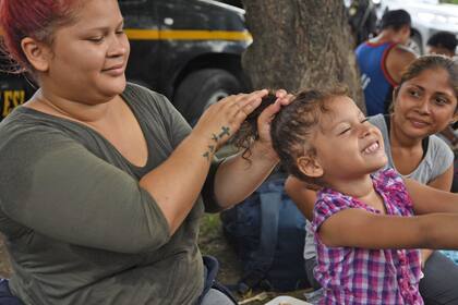 Un mujer peina a su hija en un descanso en la marcha de la caravana