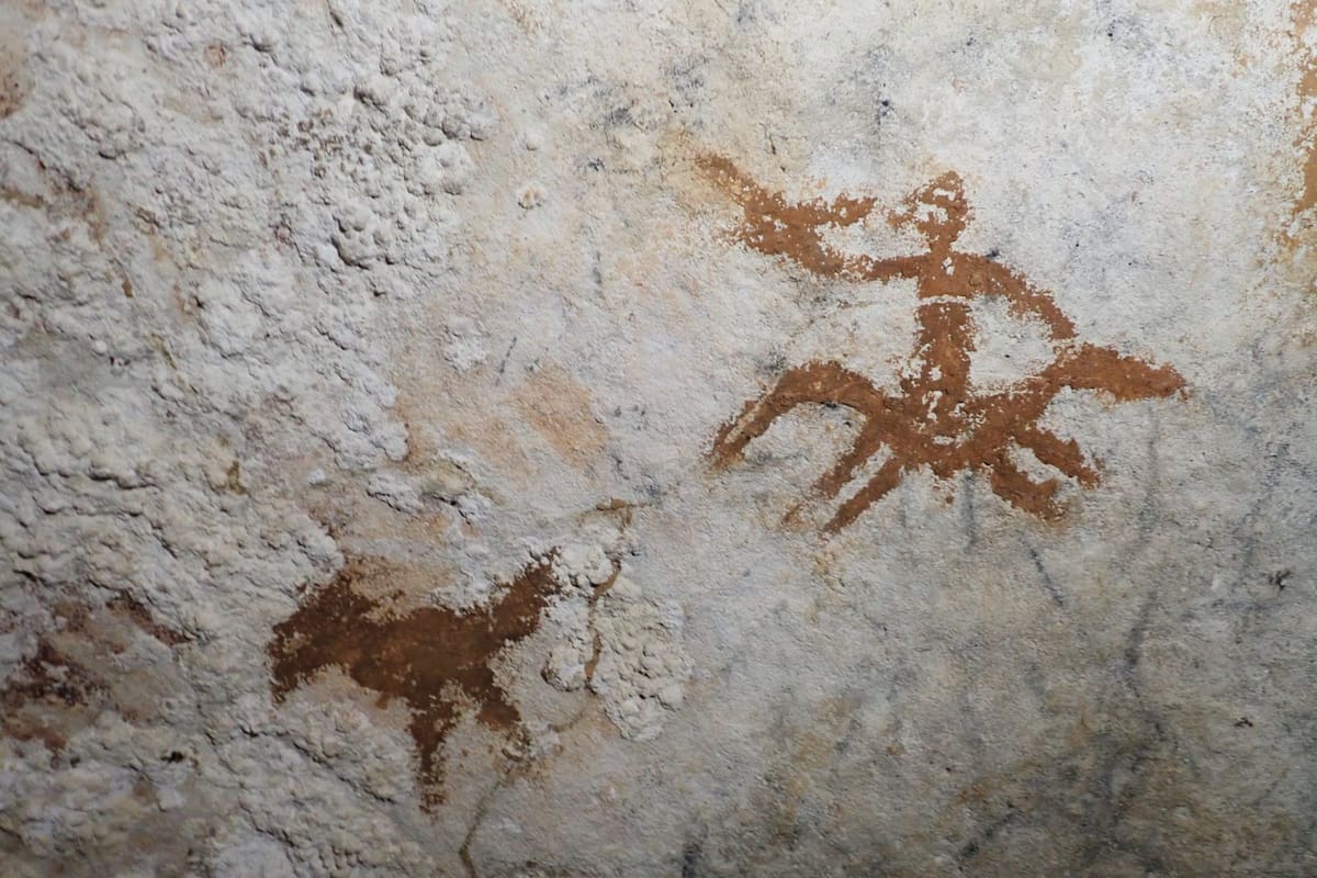 Casi imperceptible, entre las dos imágenes se halla la mano pintada hace 67.800 años