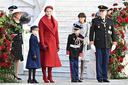 Charlene y Gabrielle apostaron a looks coordinados: tapados iguales, pero en distinto tono, de DidierAngelo. Mientras la madre le sumó botas elastizadas de gamuza Manolo Blahnik y tocado de Stephen Jones, la hija llevó zapatos de charol con taco de Louboutin. A su lado están el príncipe Alberto, su hijo Jacques y la princesa Estefanía.