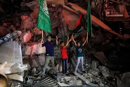 Chicos palestinos ondean la bandera verde de Hamas y la de palestina sobre los escombros de un edificio derribado mientras celebran el acuerdo de alto el fuego entre Israel y el grupo islamista, en la Ciudad de Gaza