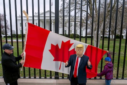 Ciudadanos canadienses despliegan su bandera frete a la Casa Blanca para mostrar su apoyo a su país, mientras otra persona usa una máscara del presidente Donald Trump