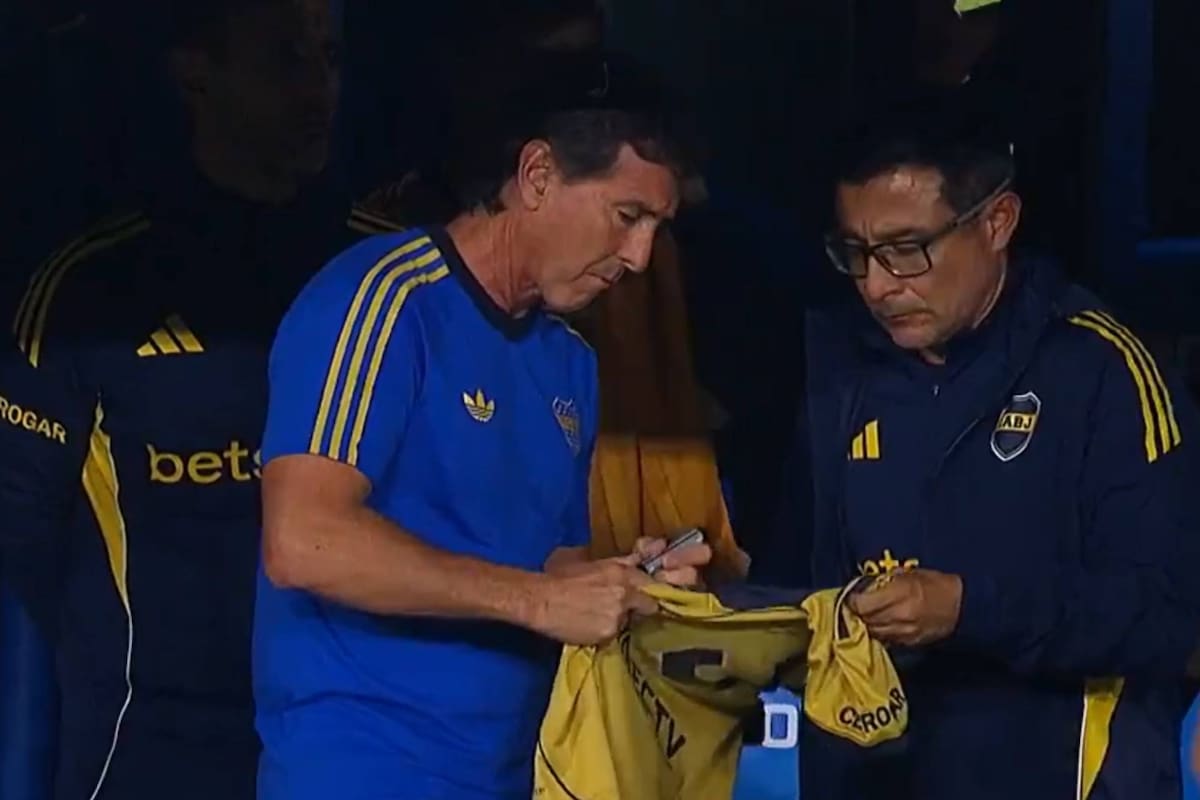 Claudio Ubeda firma la camiseta que le arrojó un hincha desde un palco; su ayudante, Juvenal Olmos, la sostiene