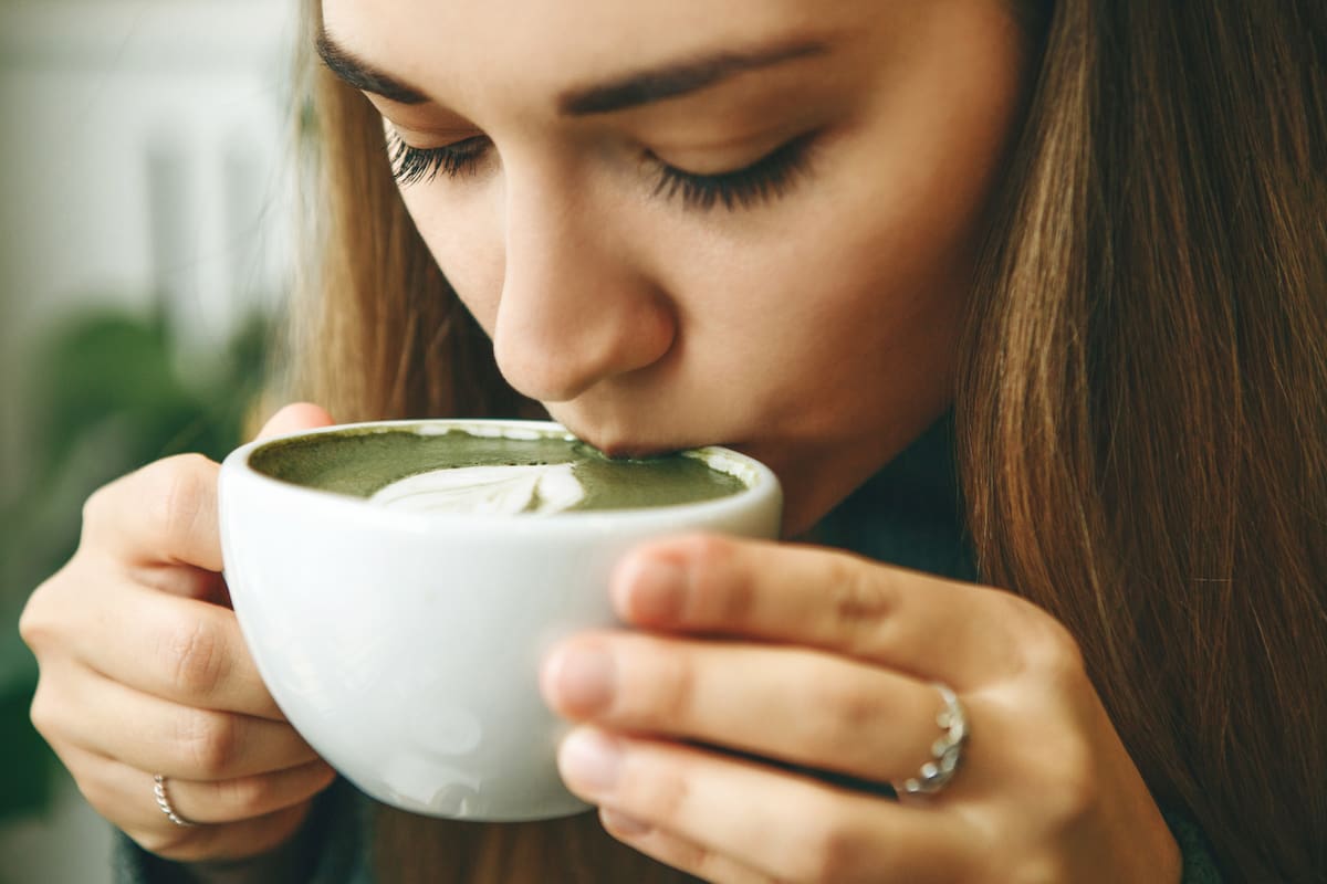 Close-up face or portrait of a girl who drinks healthy and delicious green matcha latte tea
