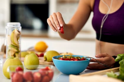 Close-up of athletic woman eating healthy and preparing fruit salad in the kitchen.