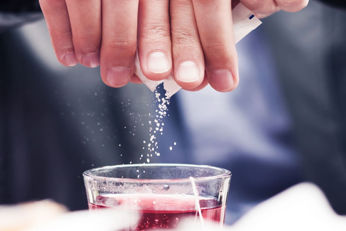 Close-up of white sugar particles falling in cup filled with tea.