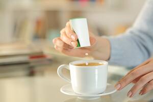 Close up of woman hand throwing saccharin pills on coffee cup on a desk at home