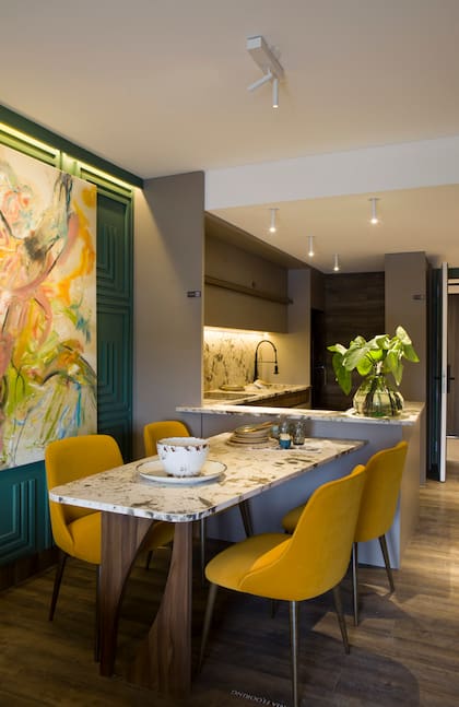 El tono mostaza de las sillas ofrece un buen contraste al verde de la pared con boiserie y la piedra de la mesa de comedor emparejada con la mesada genera una transición fluida al living.