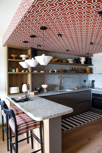 Banquetas de cocina Moller lustradas en negro y tapizadas en lana italiana y alfombra rayada blanco y negro con vivo (todo, Concepto Fusión). Horno y anafe (Teka), heladera (Drean).