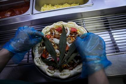 Colocan una hoja de cannabis en una pizza en un restaurante, Bangkok, Tailandia, 24 de noviembre de 2021. The Pizza Company, una gran cadena tailandesa de comidas rápidas, está promocionando su "pizza loca feliz", un producto cubierto con una hoja de cannabis. Es legal, pero no te drpga. (AP Foto/Sakchai Lalit)